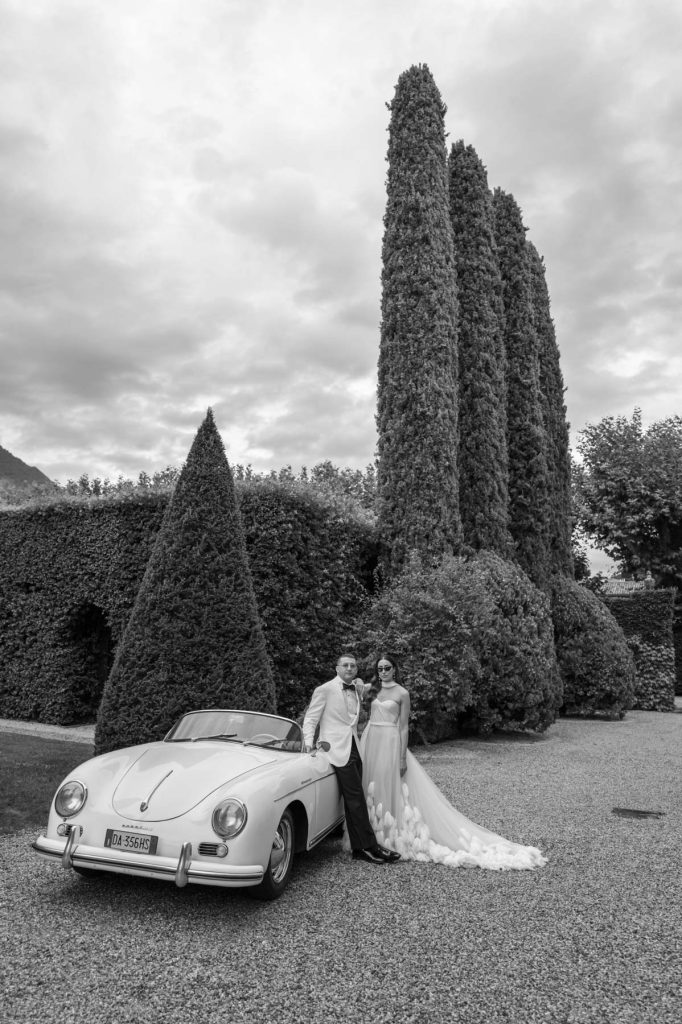 Alex and Julian stood by a vintage car following their Villa Balbiano Wedding in Lake Como