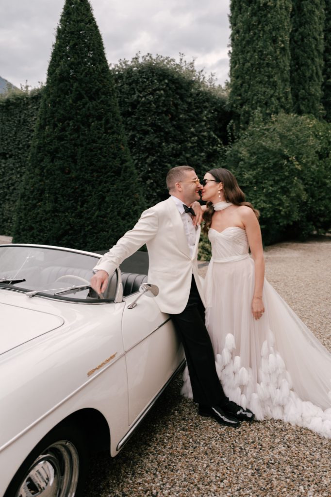 A + J enjoying a quiet moment next to a white sports car immediately after their Villa Balbiano Wedding in Lake Como