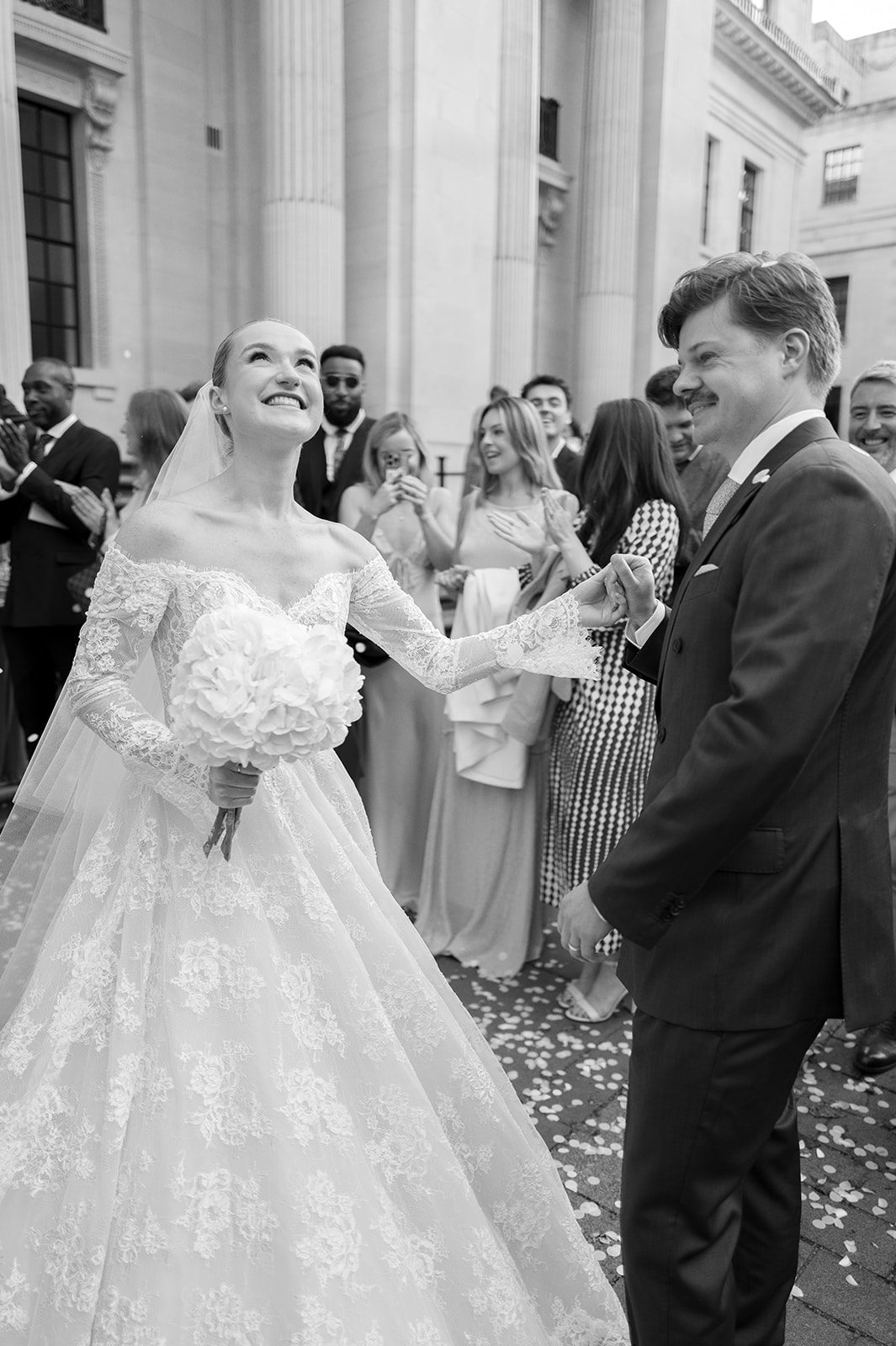 Surrounded by happy guests, a bride stands outside of Old Marylebone Town Hall looking towards the sky with a huge smile on her face.