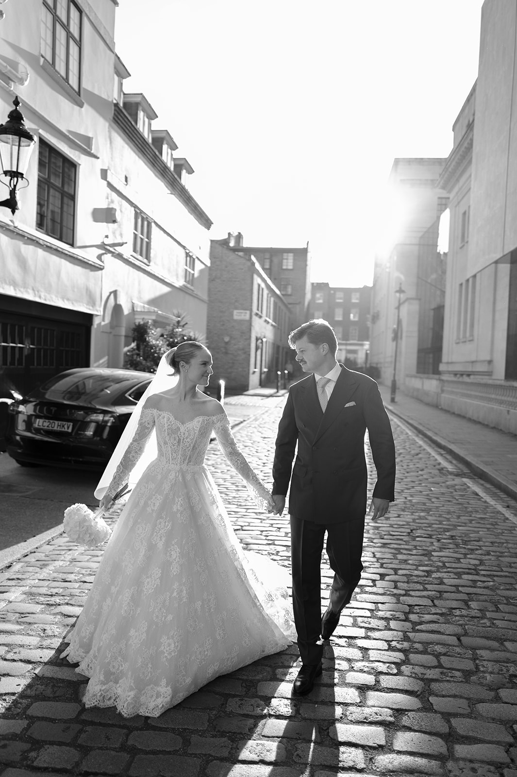 In a cobbled street in the streets behind Old Marylebone Town Hall, a couple walk towards the camera holding hands and looking into each others eyes.