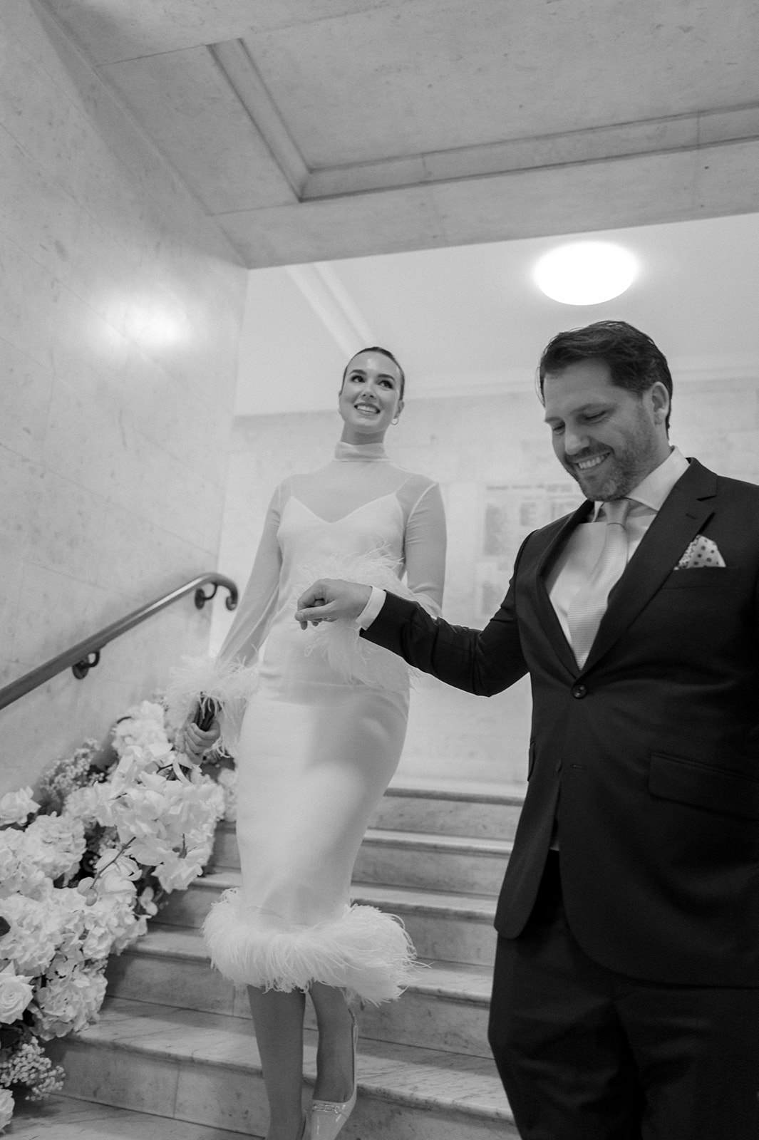 A groom can be seen laughing as he holds his new wife's hand whilst they walk cautiously down the interior steps of Old Marylebone Town Hall.