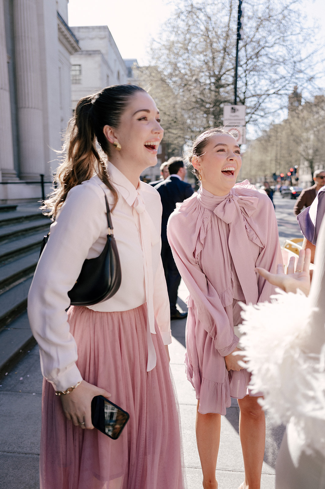 Two women wearing different subtle shades of pink can be seen laughing outside of the venue.